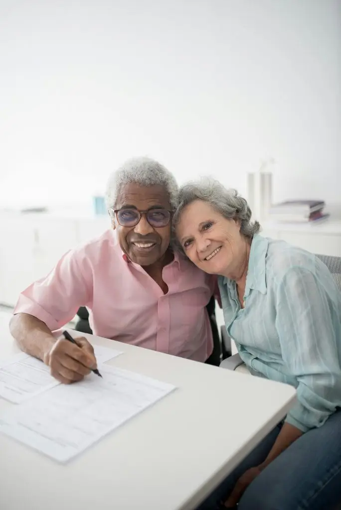 Happy elderly couple sitting at a desk, smiling and signing documents. Perfect for insurance and lifestyle themes.